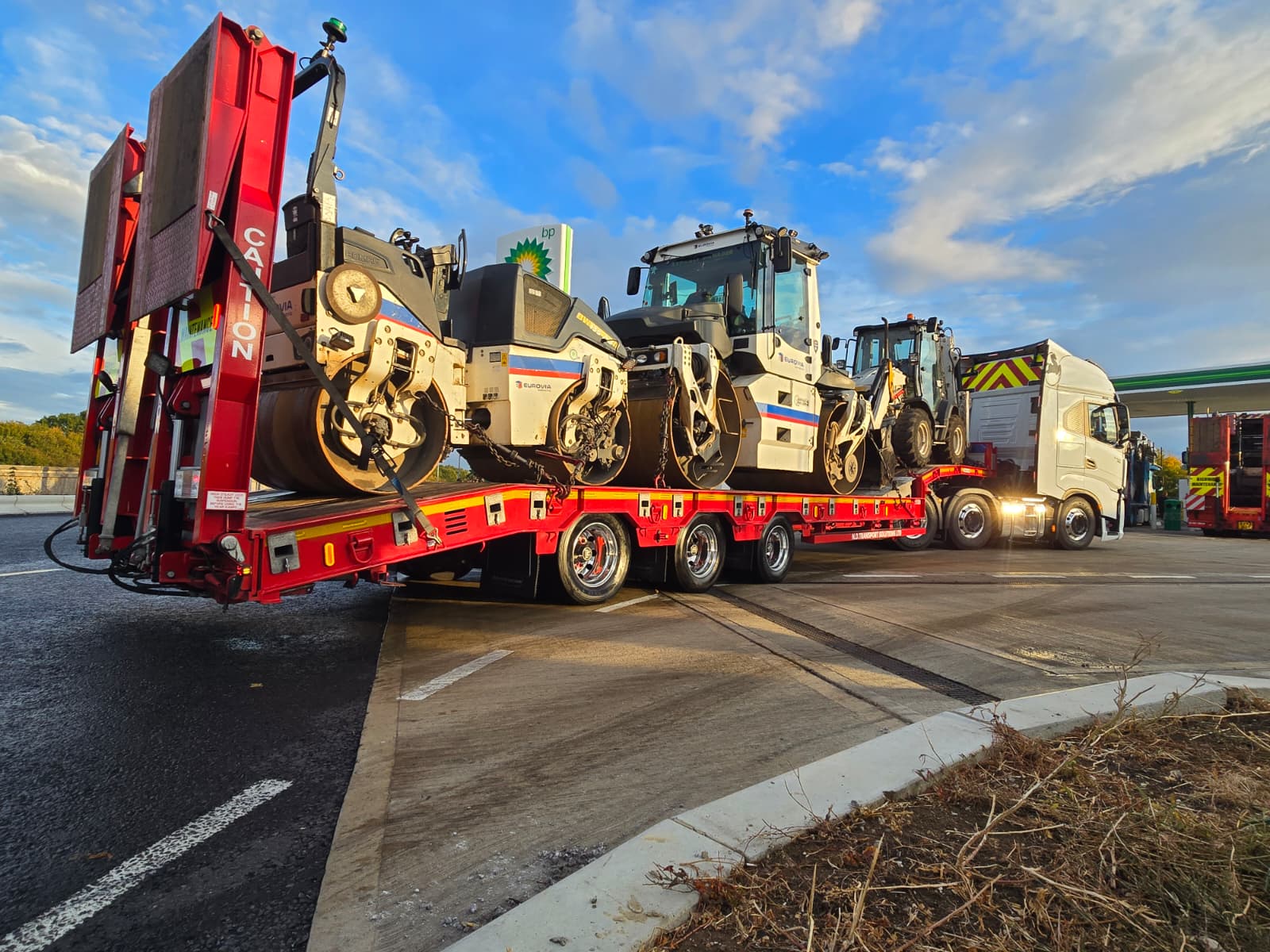 Road-surfacing plant loaded and secured on a low loader